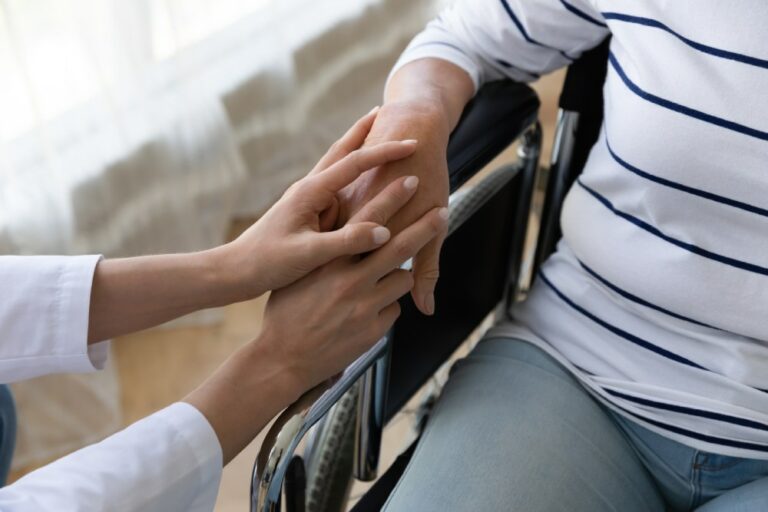 Young female nurse caregiver hold hand support disabled handicapped senior adult grandma patient sit on wheelchair
