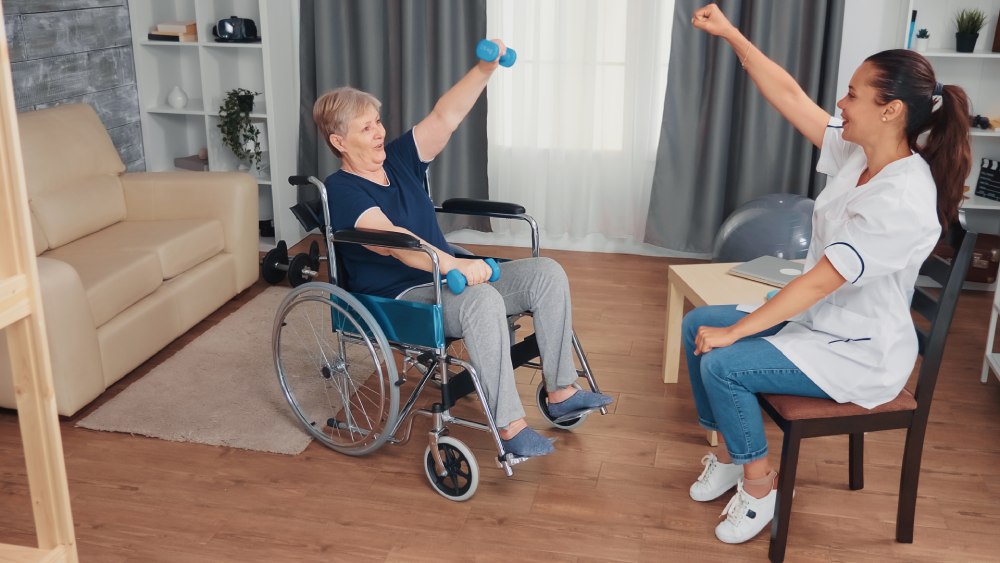 Invalid grandmother in wheelchair doing recovery therapy with doctor.